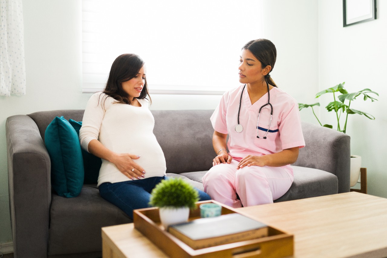 Stressed expectant mother called in a professional midwife nurse because of her pain.  Worried pregnant woman having strong pain and problems with her pregnancy