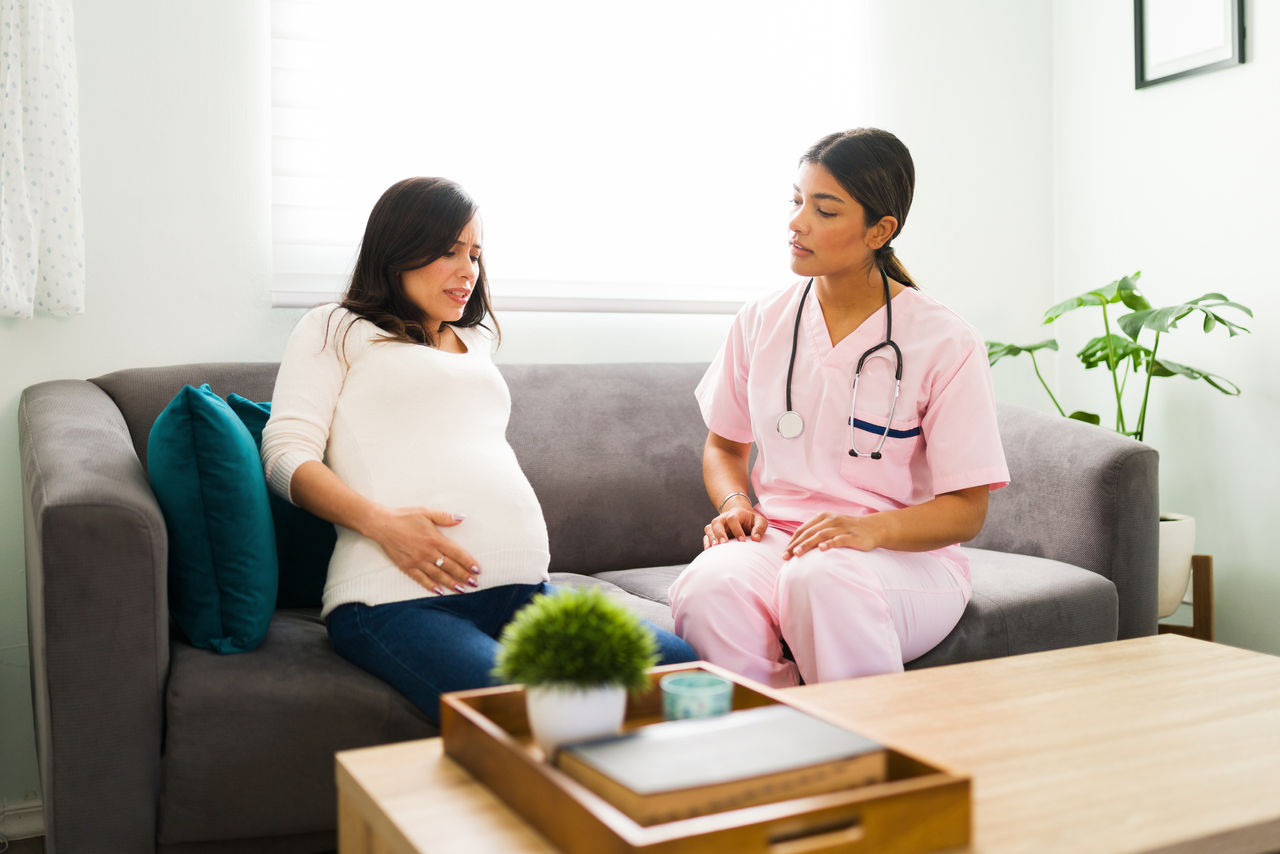 Stressed expectant mother called in a professional midwife nurse because of her pain.  Worried pregnant woman having strong pain and problems with her pregnancy