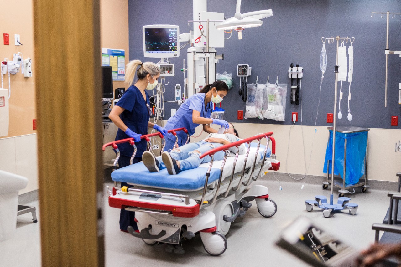 A view through the open door of an emergency examination room as two female nurses stabilize the female patient.