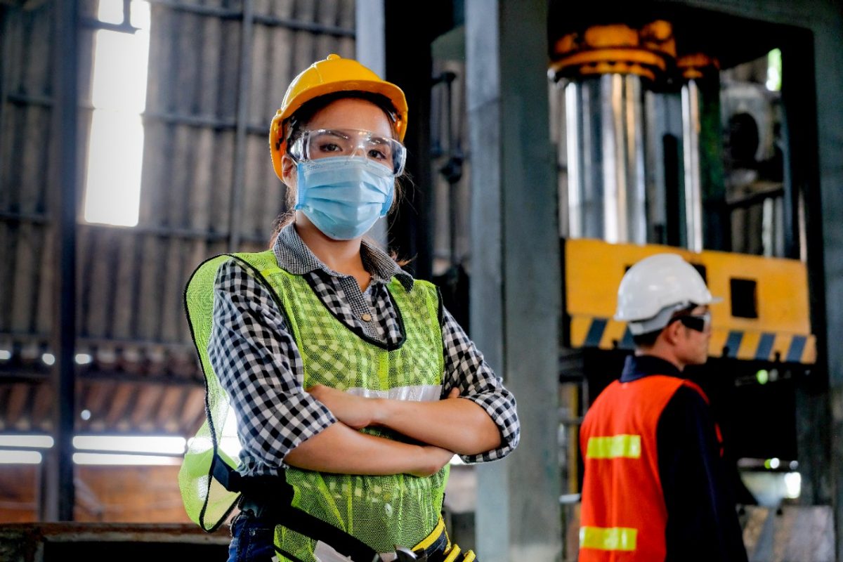 Factory woman worker or technician with hygienic mask stand with confident action with her co-worker  as background.