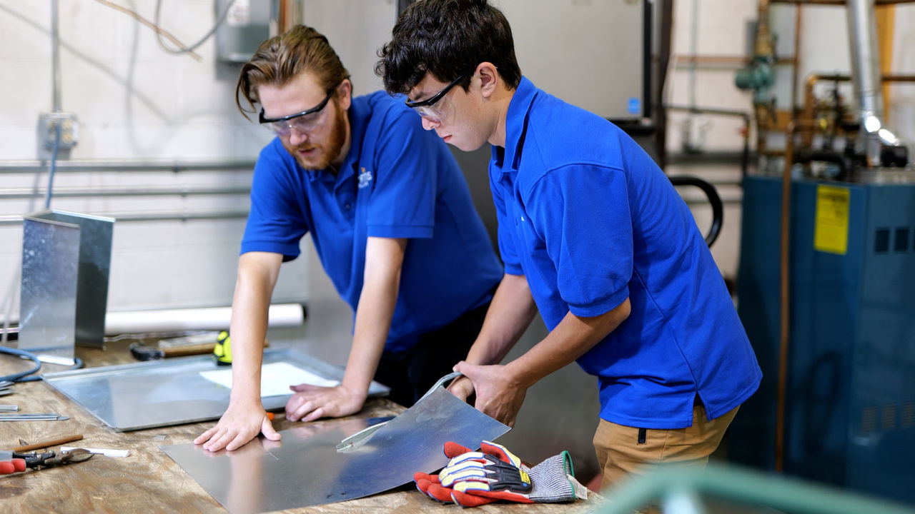 Two workers shaping metal sheet in workshop